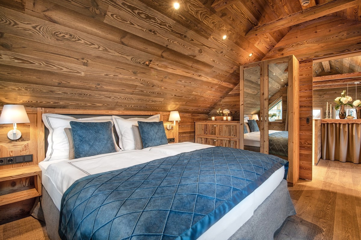 Un dormitorio con paneles de madera, una cama grande, mesitas de noche y un espejo.