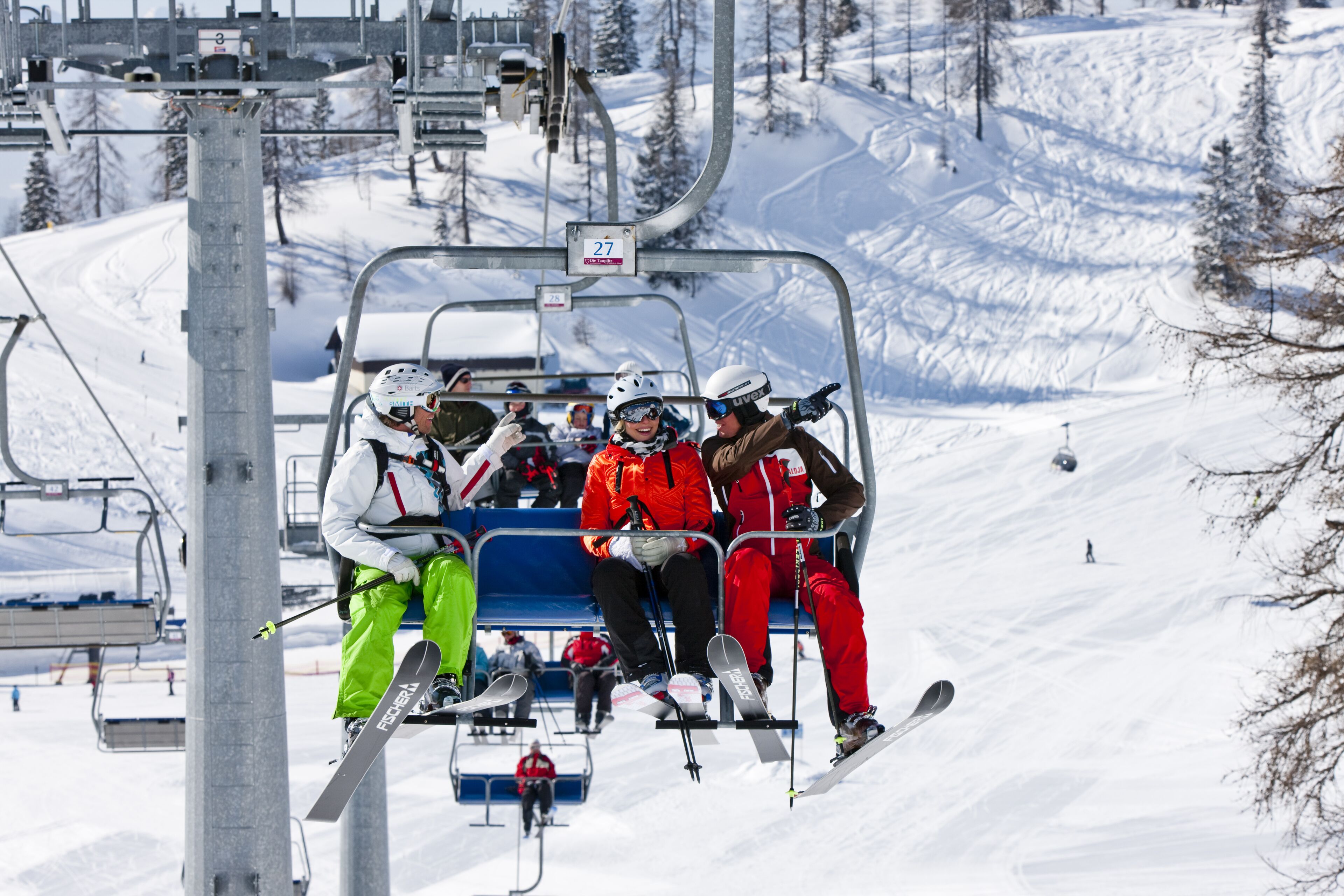 A ski lift with passengers wearing helmets and ski gear.