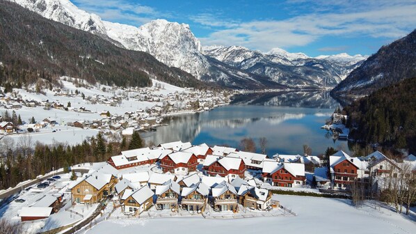 Un pueblo cubierto de nieve con casas de madera tradicionales, un lago y montañas al fondo.