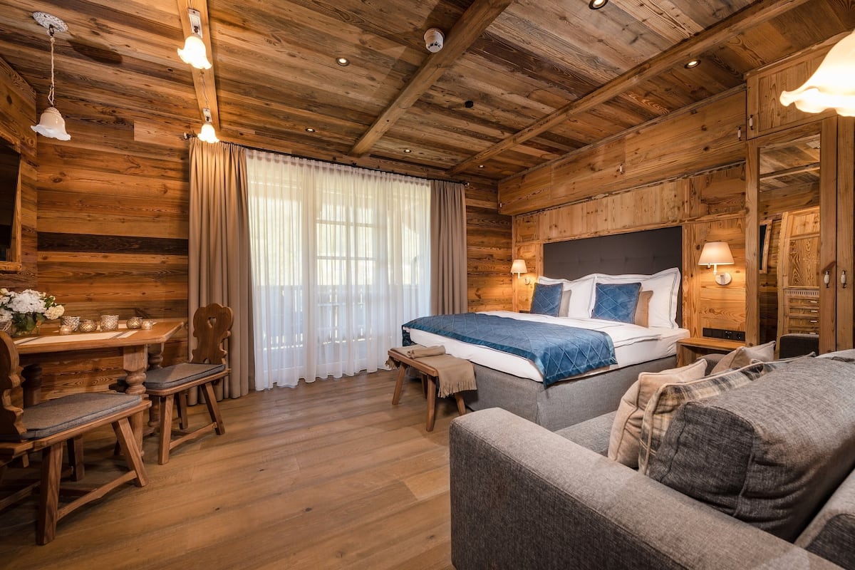 Una habitación tipo cabaña de madera con una cama, un sofá, una mesa de comedor con sillas y una mesita con un florero.