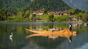 Ein ruhiger See mit einem Holzboot, einem Schwan und Häusern im Hintergrund.