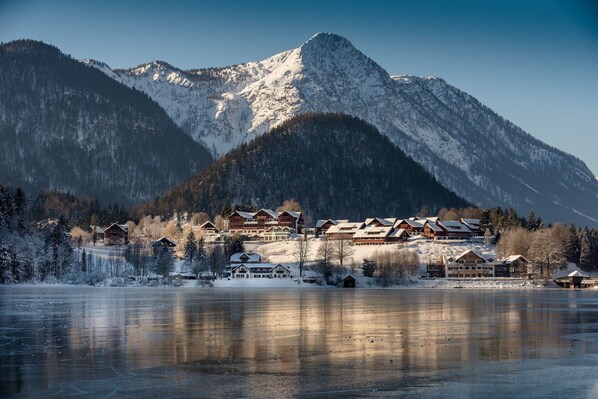 A mountain lodge with multiple buildings, a frozen lake in the foreground, and snow-covered trees.