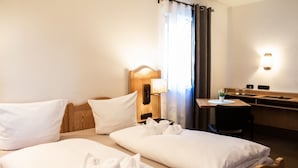 Habitación de hotel con dos camas, un escritorio, una silla, una lámpara y una ventana con cortinas.