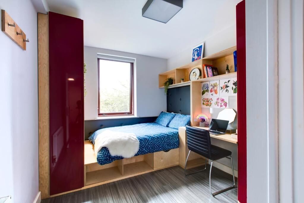 A compact bedroom with a bed, desk, and shelving unit.