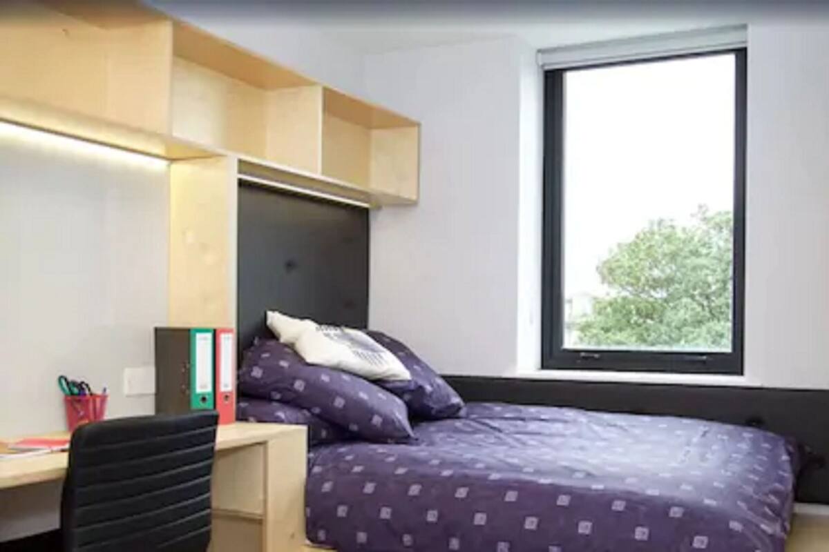 A bedroom with a bed, a desk, and a window.