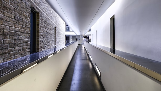 A long, narrow corridor with a brick wall on one side and a white wall on the other, leading to a staircase. - Yugo Explore - Broadstone Hall (Dublin)