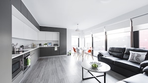A modern kitchen with grey cabinets, a dining area with a table and chairs, and a living area with a sofa and a coffee table. - Yugo Explore - Broadstone Hall (Dublin)