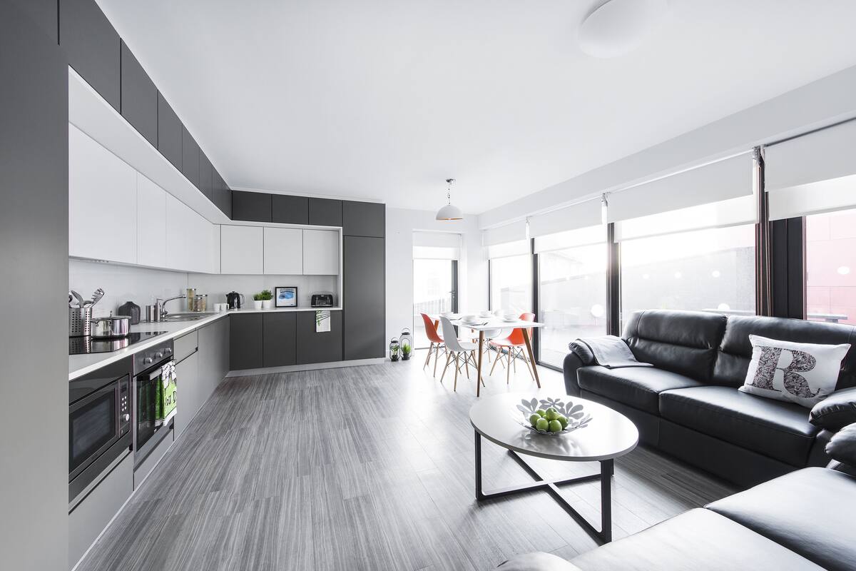 A modern kitchen with grey cabinets, a dining area with a table and chairs, and a living area with a sofa and a coffee table.