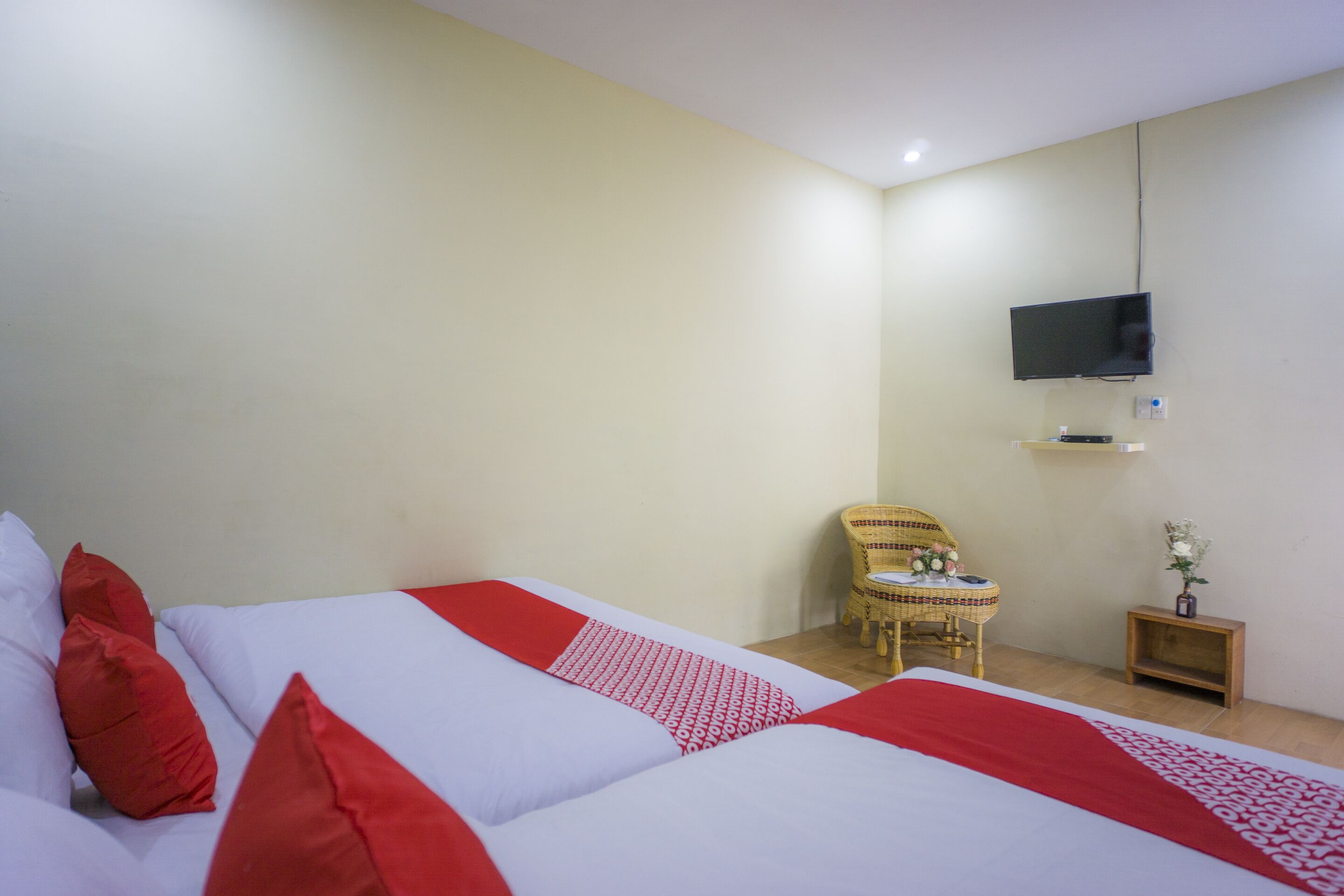 A hotel room with a large bed, a television mounted on the wall, a small table with a chair, and a nightstand with a vase.