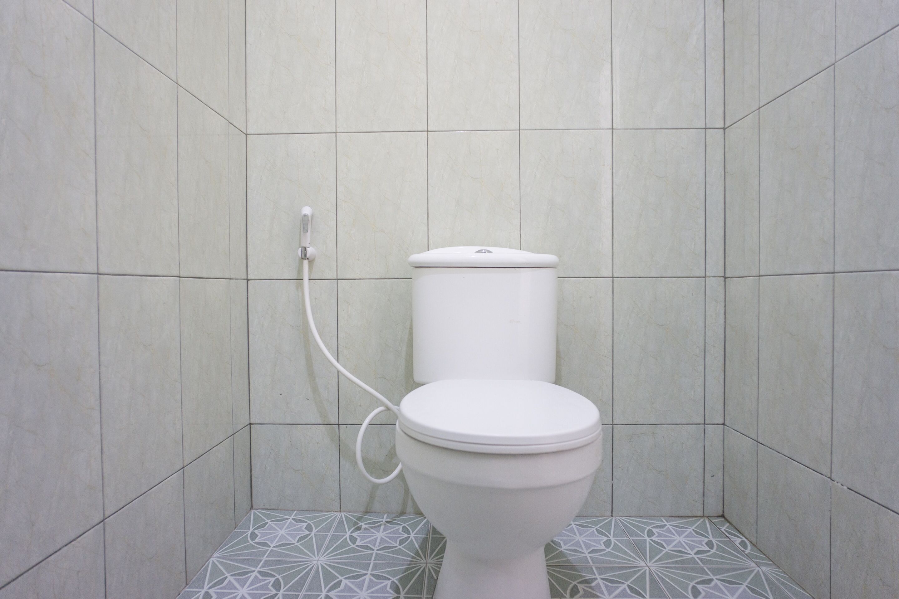 A bathroom with a toilet, tiled walls, and a geometric patterned floor.