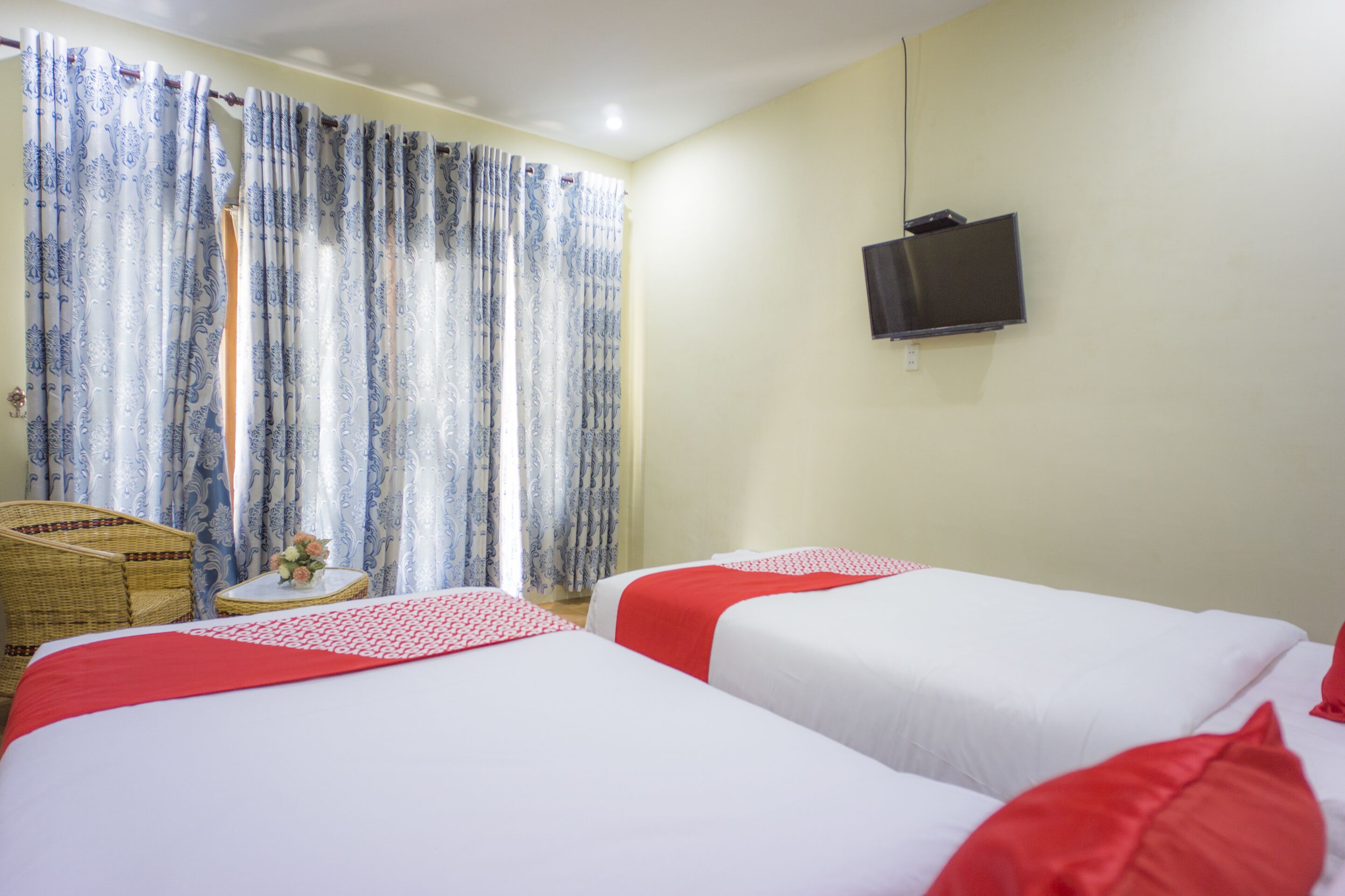Een hotelkamer met twee bedden, een aan de muur bevestigde televisie en een rieten stoel.