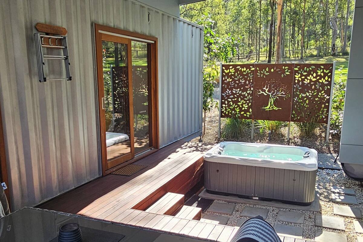 A modern outdoor deck with a hot tub, a wicker sofa, and a glass table.