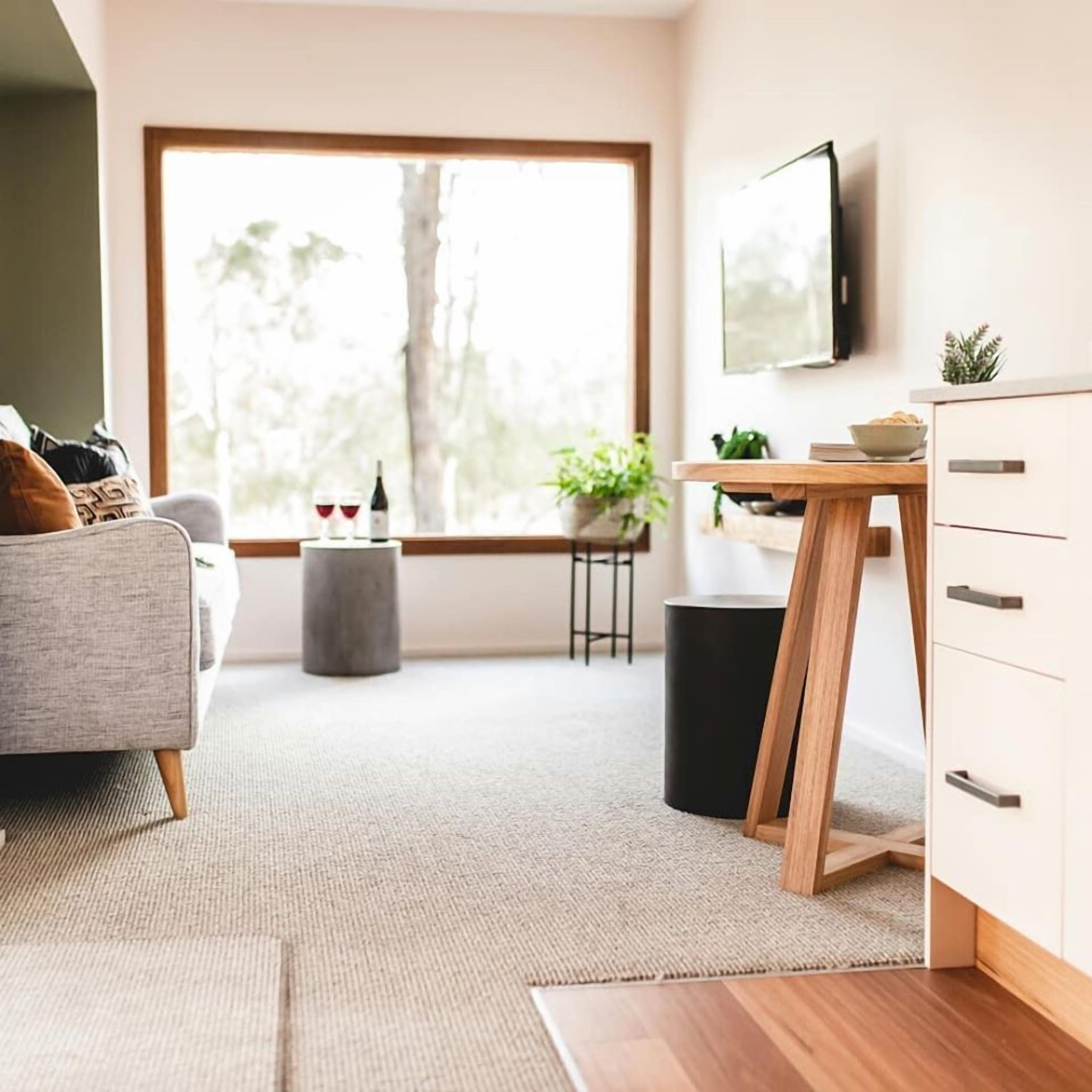 Un salon moderne comprenant un canapé, une table basse, un téléviseur fixé au mur, une table à manger avec des chaises et une grande fenêtre donnant sur un paysage arboré.