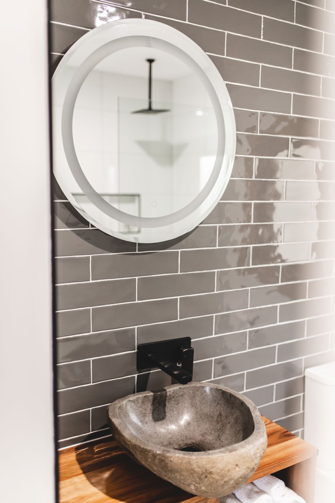 A bathroom with a modern design, featuring a round mirror and a stone sink.