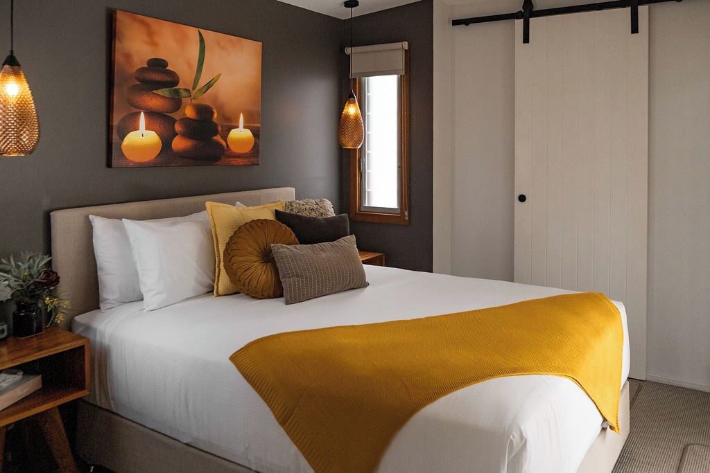 A neatly made bed with a white comforter and a mustard-colored throw blanket.