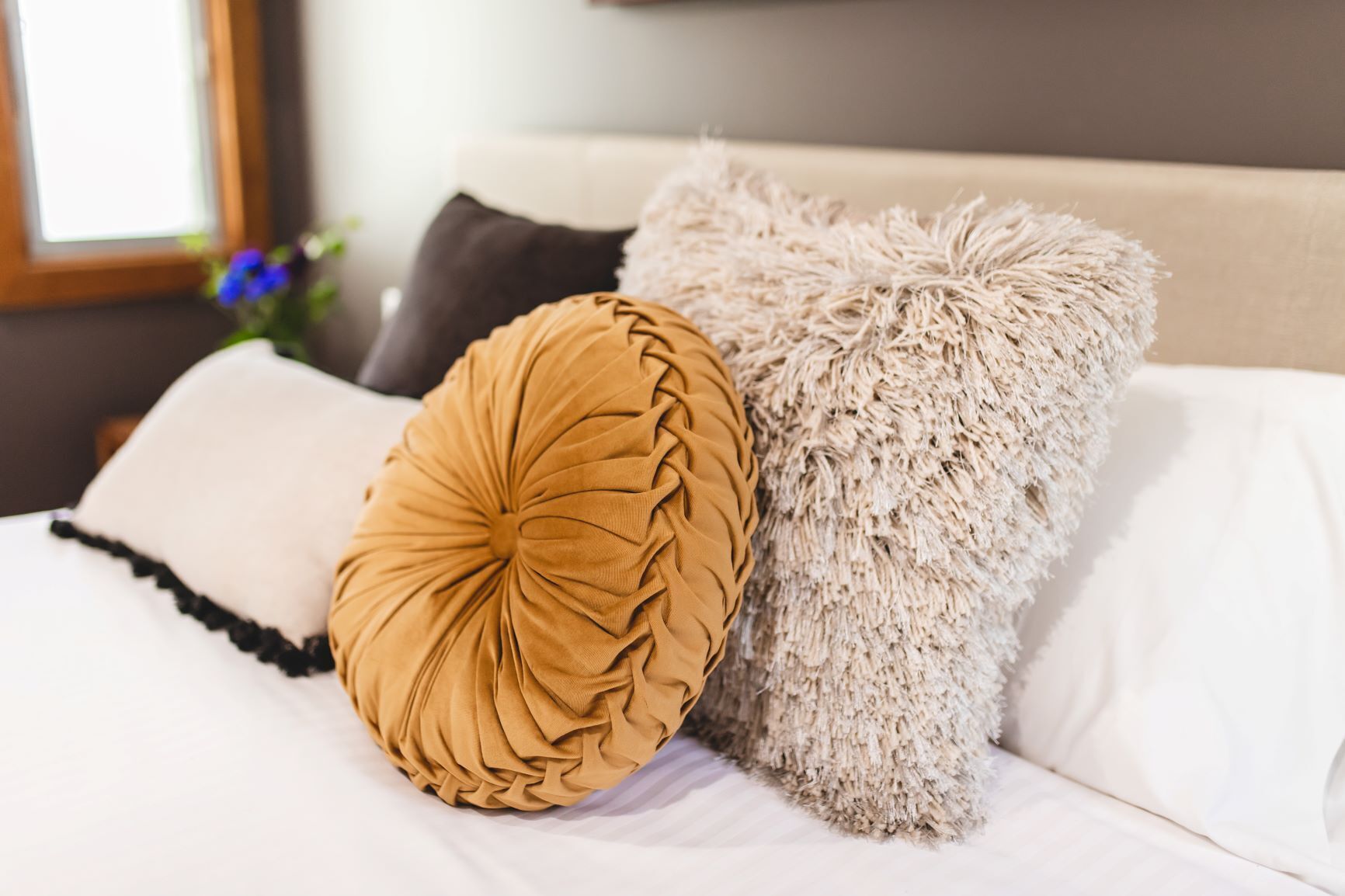 A bed with a white sheet, a brown decorative pillow, and a fluffy beige throw.