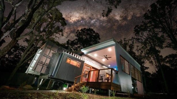A modern house with a deck and a starry night sky visible through the windows. - Tuckers Lane Boutique Accommodation (North Rothbury)