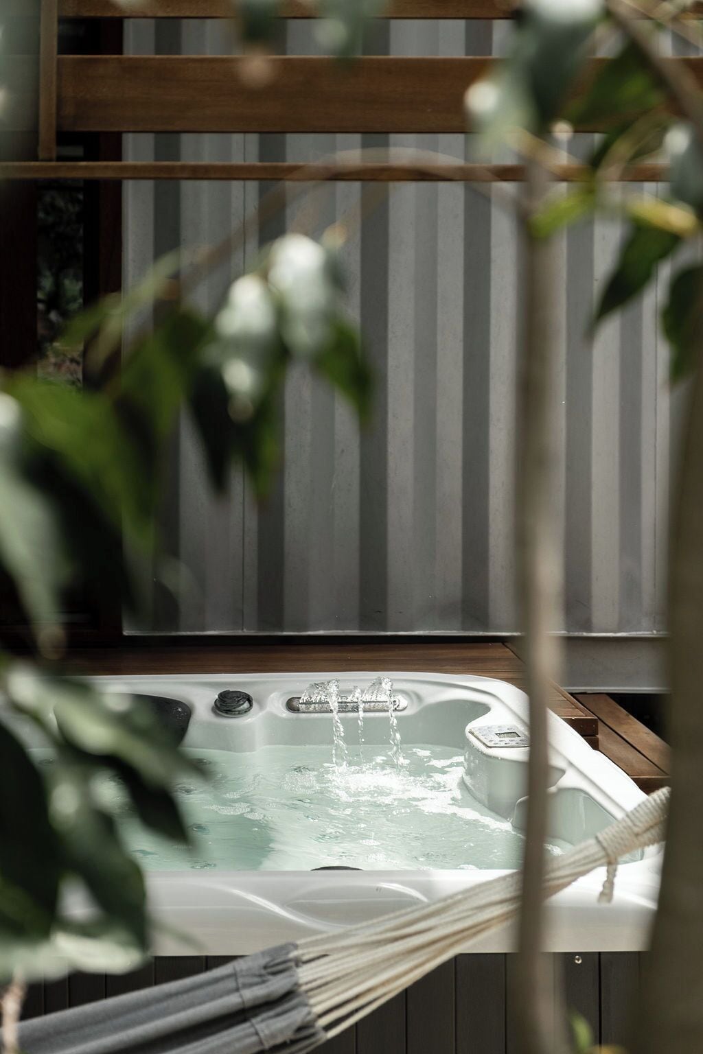 A hot tub with water flowing, surrounded by wooden beams and a hammock.