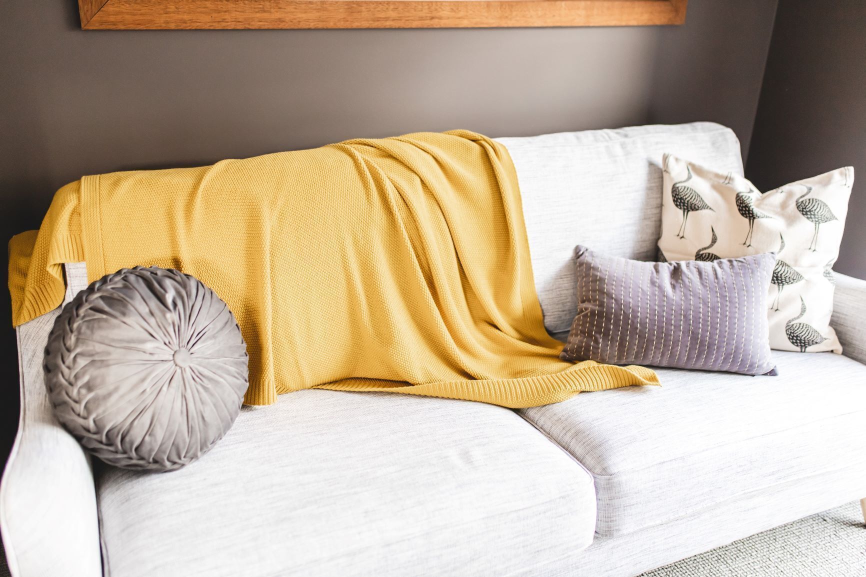 A white sofa with a mustard yellow blanket and patterned pillows.