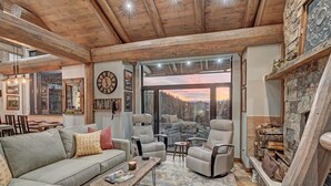 Una sala de estar acogedora con un ventanal que ofrece vistas panorámicas, una chimenea con leña y un comedor con mesa y sillas de madera.