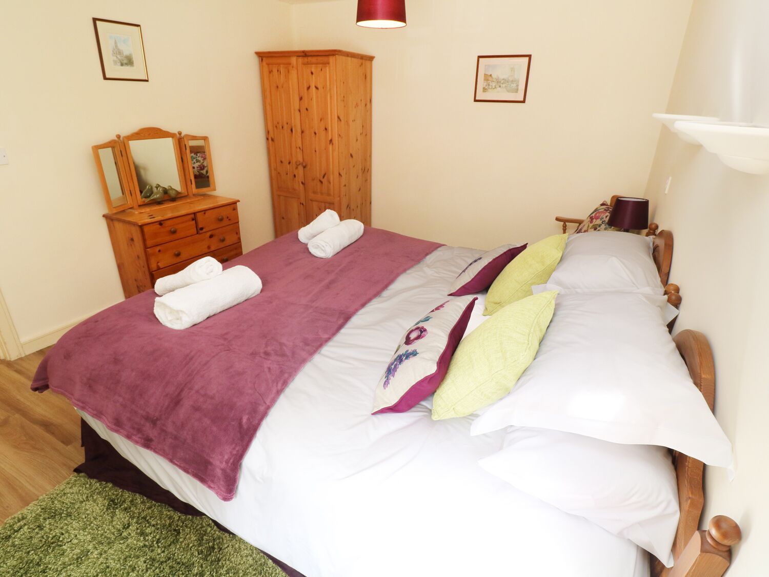 A neatly made bed with a purple blanket, white pillows, and a green rug.