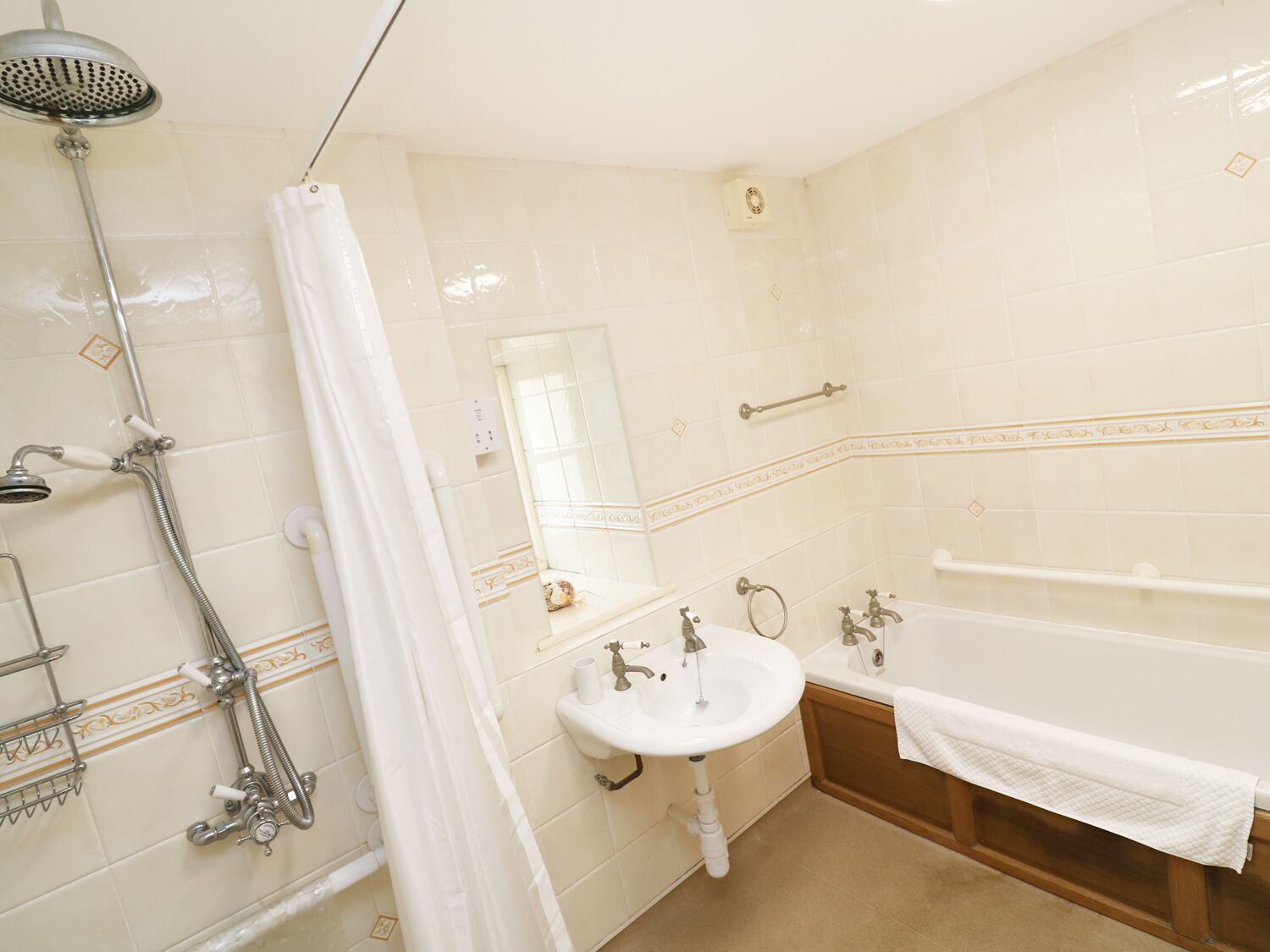 Un baño con ducha, lavamanos y bañera, todo con sanitarios blancos y azulejos color beige.