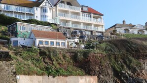 Un bâtiment situé sur la côte, doté de nombreux balcons, d’un mur de soutènement en pierre et d’une plage de sable au premier plan.