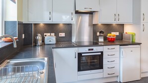 Une cuisine moderne avec des armoires blanches, une hotte de cuisinière en acier inoxydable, un four encastré et un plan de travail sur lequel se trouvent une bouilloire et un grille-pain.