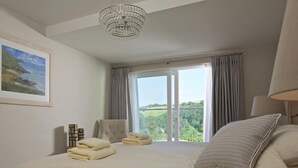 A bedroom with a large bed, a view of greenery through the window, and a chandelier. - 2 Hamstone Court (Salcombe)