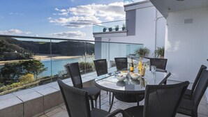 A round glass table with six chairs on a balcony overlooking a beach and sea. - 2 Hamstone Court (Salcombe)