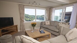 A living room with a sofa, a coffee table, a TV, and a window with a view of greenery. - 2 Hamstone Court (Salcombe)