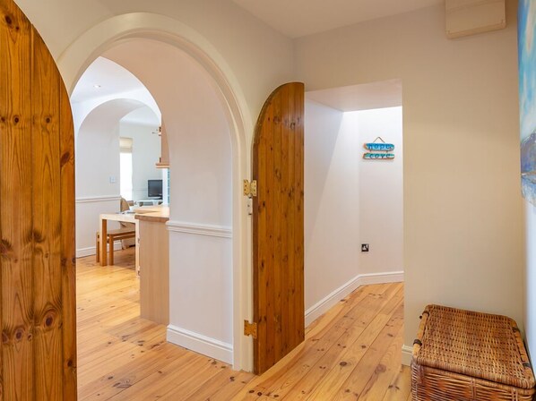 A hallway with wooden flooring, white walls, and a wooden door. There is a wicker chair and a sign that reads "hope and love" on the wall. - 2 Armada House (Kingsbridge)
