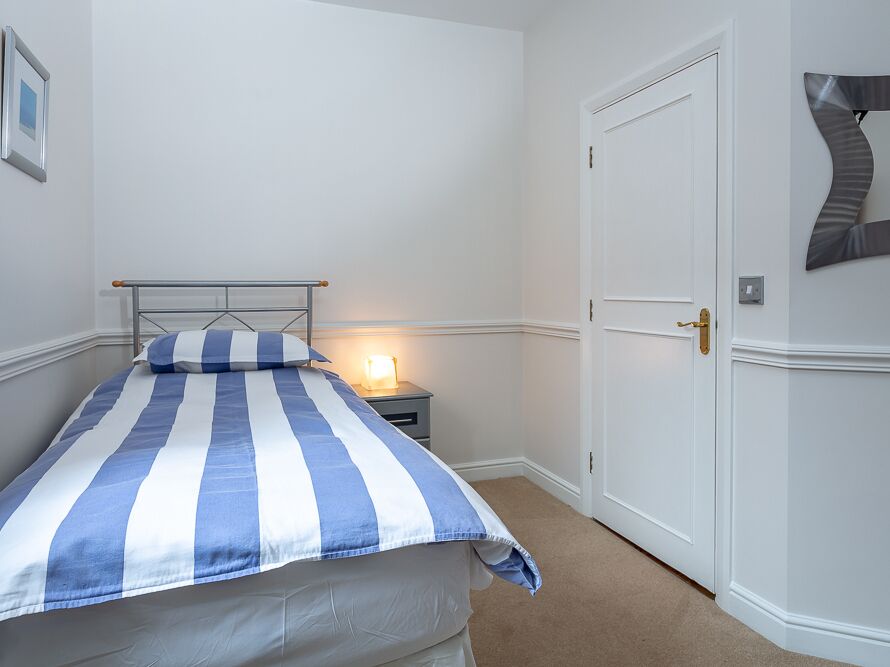 A bedroom with a bed, a nightstand, a door, and a wall-mounted mirror.