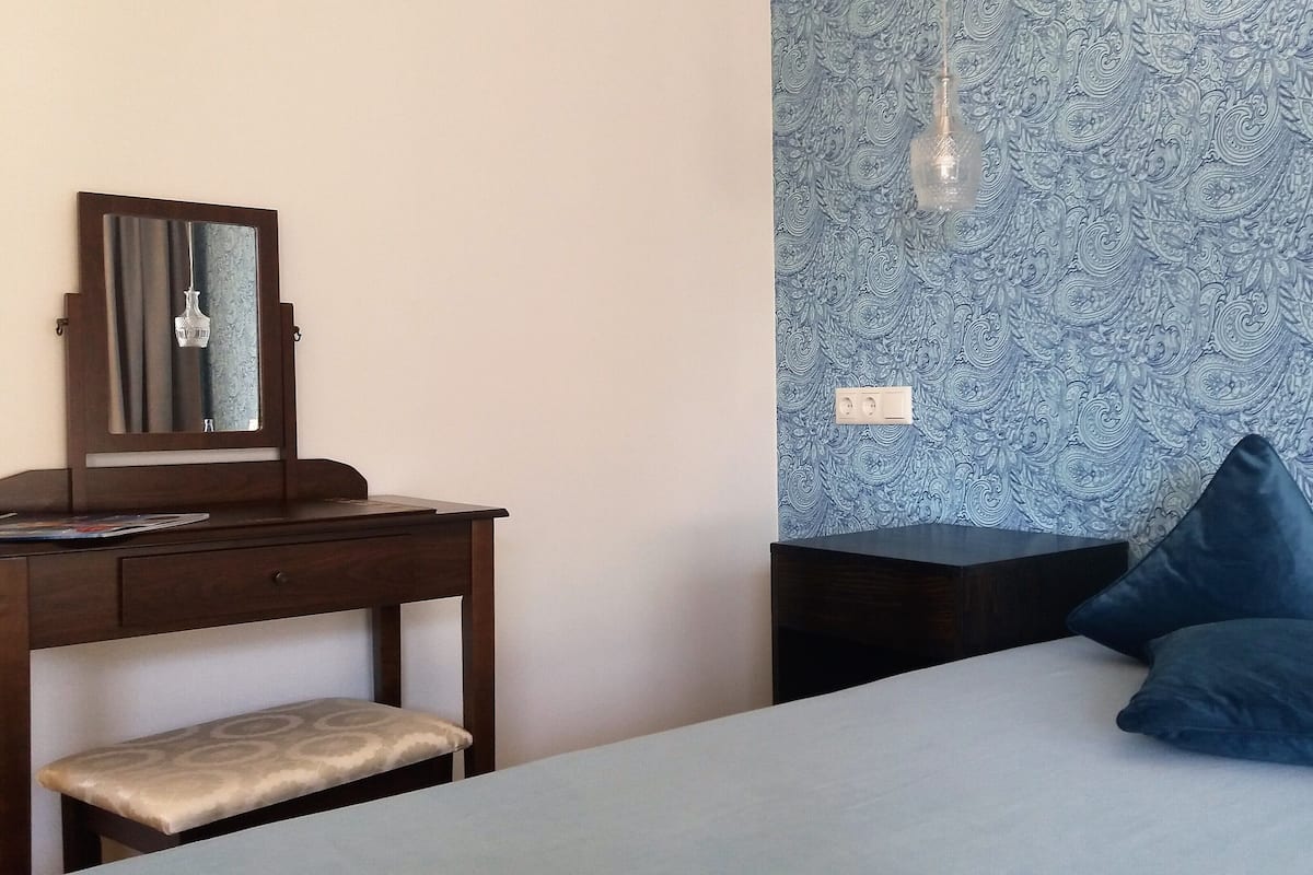 A bedroom with a bed, a bedside table, a dresser, a mirror, and a patterned wall.