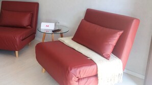 A red sofa with a white throw blanket and a glass table with a remote control and a sign. - Motel Zur goldenen Krone (Teterow)