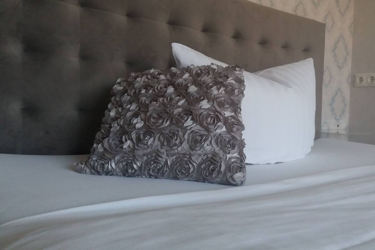 A bed with a tufted headboard, a white pillow, and a decorative pillow with a floral pattern.