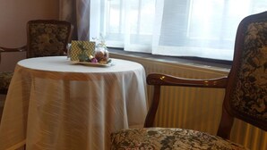 A dining area with a round table covered by a white tablecloth, two chairs with floral upholstery, and a window with sheer curtains. - Motel Zur goldenen Krone (Teterow)