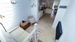 A modern kitchen with white cabinets, a dining area with a wicker chair, and a view of the adjacent living space. - Porth House with south facing courtyard garden! (St Ives)