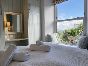 Une chambre d’hôtel avec un grand lit, un miroir, une fenêtre donnant sur des palmiers et un immeuble, ainsi qu’une table de chevet avec une lampe.