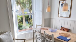 A dining area with a wooden table, white chairs, a blue bowl, and a woven placemat. - Porth House with south facing courtyard garden! (St Ives)