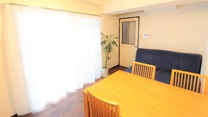 A room with a wooden table and chairs, a dark sofa, a potted plant, and a door with a mirror. - Okamura Mansion (Osaka)