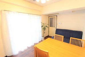 Una habitación con una mesa y sillas de madera, un sofá oscuro, una planta en maceta y una puerta con espejo.