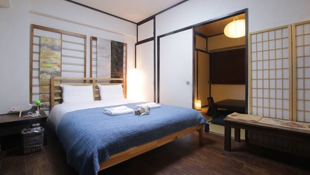A hotel room with a bed, a nightstand, a desk, and a traditional Japanese sliding door. - Okamura Mansion (Osaka)