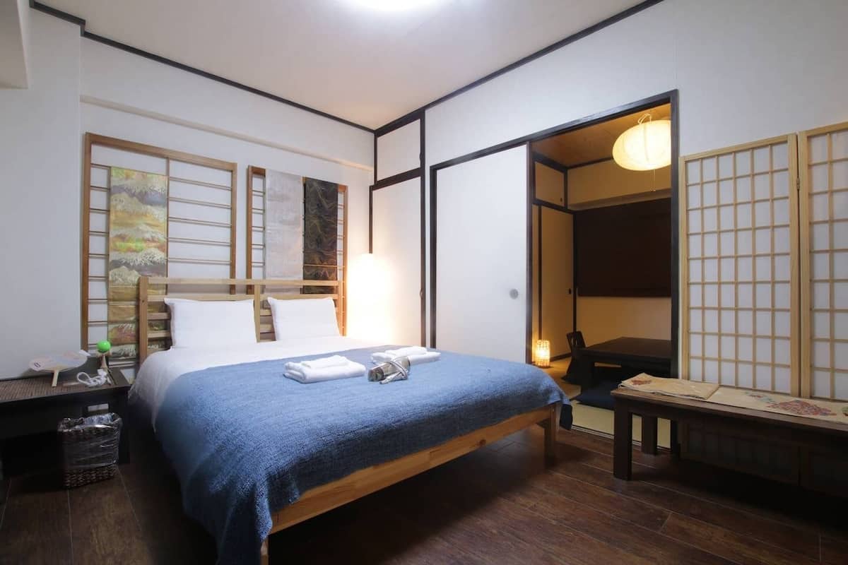 A hotel room with a bed, a nightstand, a desk, and a traditional Japanese sliding door.