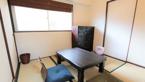 A traditional Japanese room with tatami flooring, a low table with cushions, a futon bed, and a sliding door. - Okamura Mansion (Osaka)