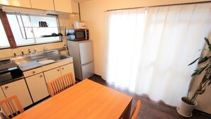 A compact kitchen with a wooden table and chairs, a microwave, and a refrigerator. - Okamura Mansion (Osaka)