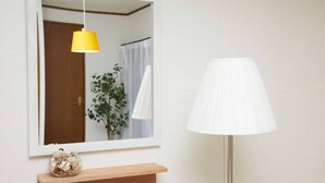 Un baño con espejo, una lámpara colgante amarilla, una lámpara blanca y un estante de madera con un tarro de vidrio.
