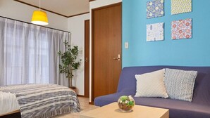 Una habitación con cama, sofá, una mesita y una planta en maceta.
