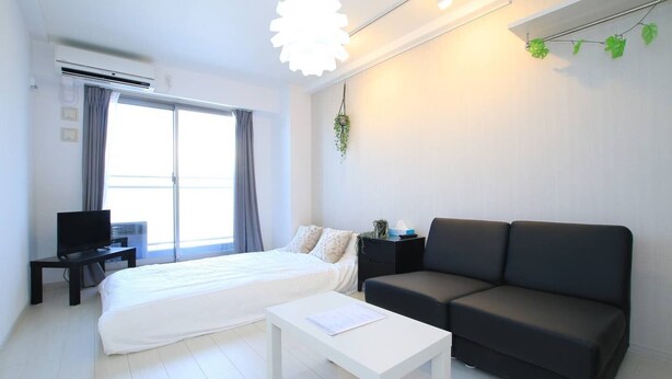 A modern hotel room with a bed, a black sofa, a white coffee table, and a TV on a small table. - Prosper Rainbow Villa (Osaka)