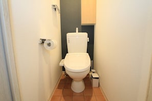A small bathroom with a toilet, a paper towel holder, and a trash bin. - Prosper Rainbow Villa (Osaka)